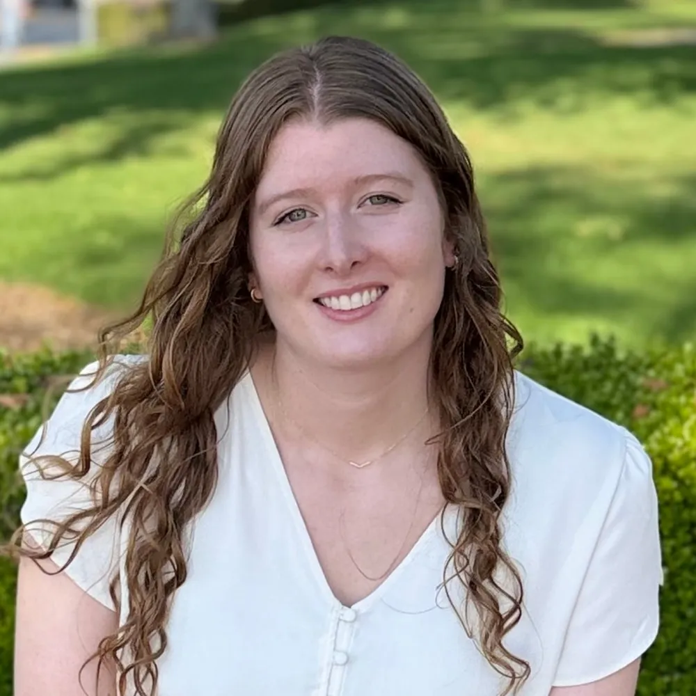 Sarah Hoogerwerf outdoors, smiling, with a green hedge behind her